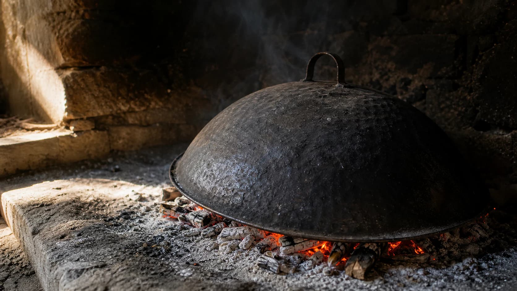 Saç tradicional i nxirë pranë prushit dhe hirit në një vatër rustike.